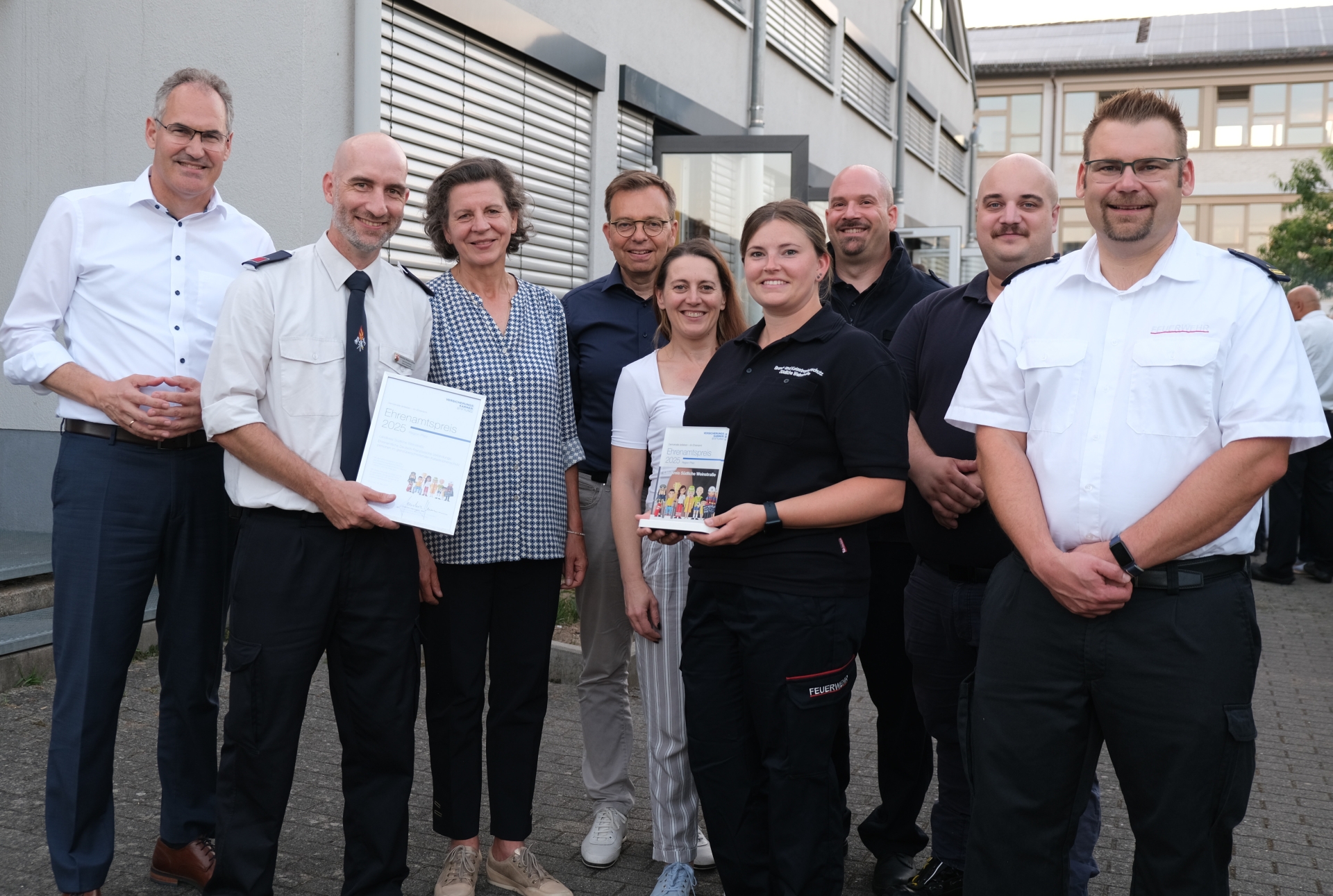 Mehrere Personen im Halbkreis, zwei Menschen halten je eine Urkunde und eine Stele, den Preis, in der Hand.