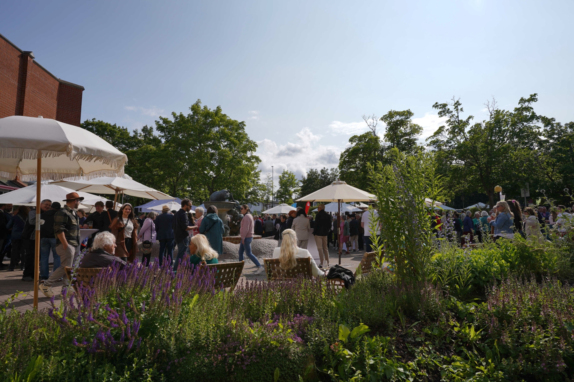 Menschen in Liegestühlen und stehend in Gruppen unter Sonnenschirmen.