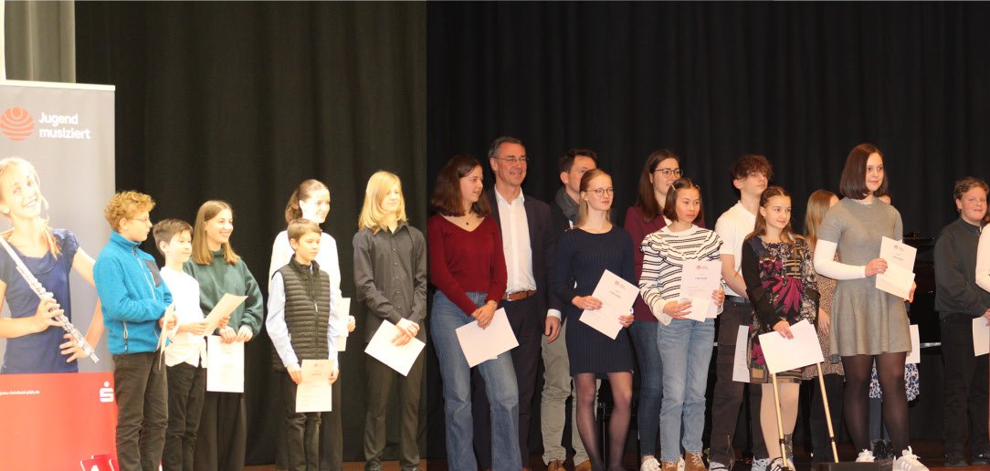 Eine große Gruppe von Kindern, Jugendlichen und Erwachsenen steht auf einer Bühne in der Germersheimer Stadthalle. Viele halten Urkunden in den Händen. Links im Bild ist ein Banner mit der Aufschrift „Jugend musiziert“ zu sehen. Die Aufnahme entstand bei der Abschlussveranstaltung des Regionalwettbewerbs Südpfalz zum 62. Wettbewerb „Jugend musiziert“.