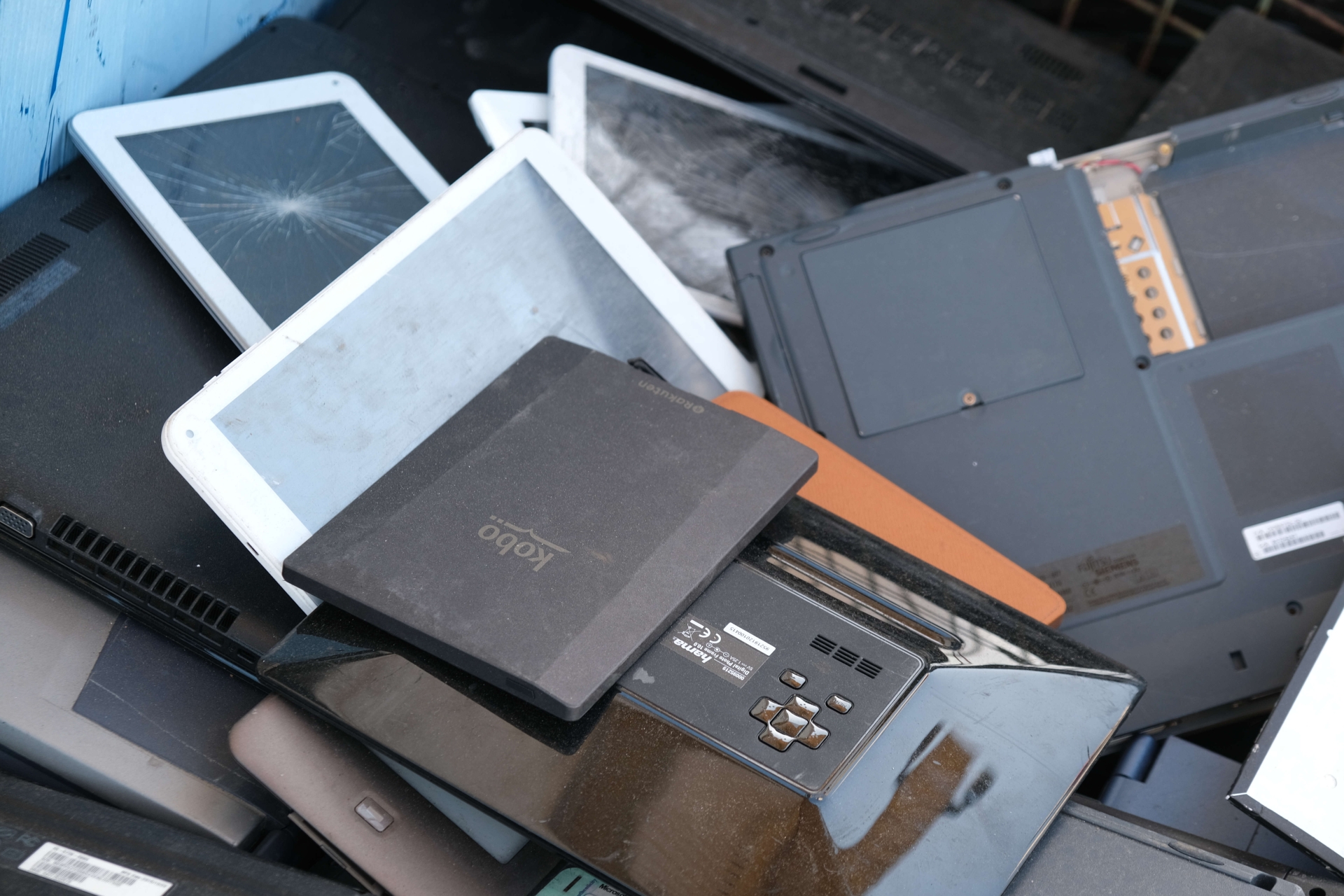 Ein Stapel Elektroschrott, in dem unter anderem mehrere Tablets zu erkennen sind, deren Bildschirme teilweise gesprungen sind.