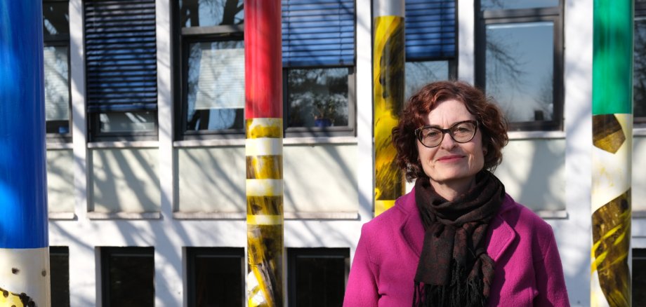 Die Künstlerin Elke Pfaffmann vor ihrem Werk „Säulen der Gesellschaft“. Foto: KV SÜW Frau vor Gebäude und bunten Stelen.