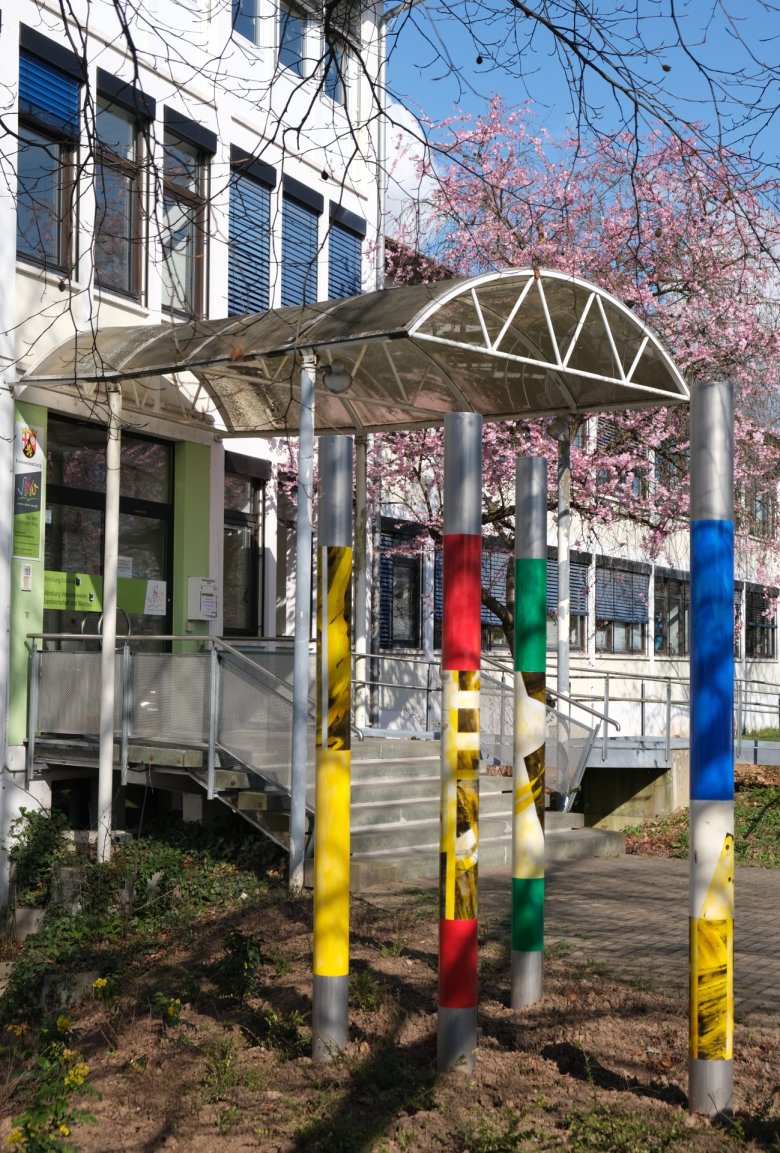 Nun realisiert: Vier grazile Edelstahlsäulen bilden zusammen das Werk „Säulen der Gesellschaft“ von Elke Pfaffmann am Eingang des Dienstgebäudes 2 der Kreisverwaltung. Foto: KV SÜW Blick zu einem Gebäudeeingang in der Arzheimer Straße in Landau.