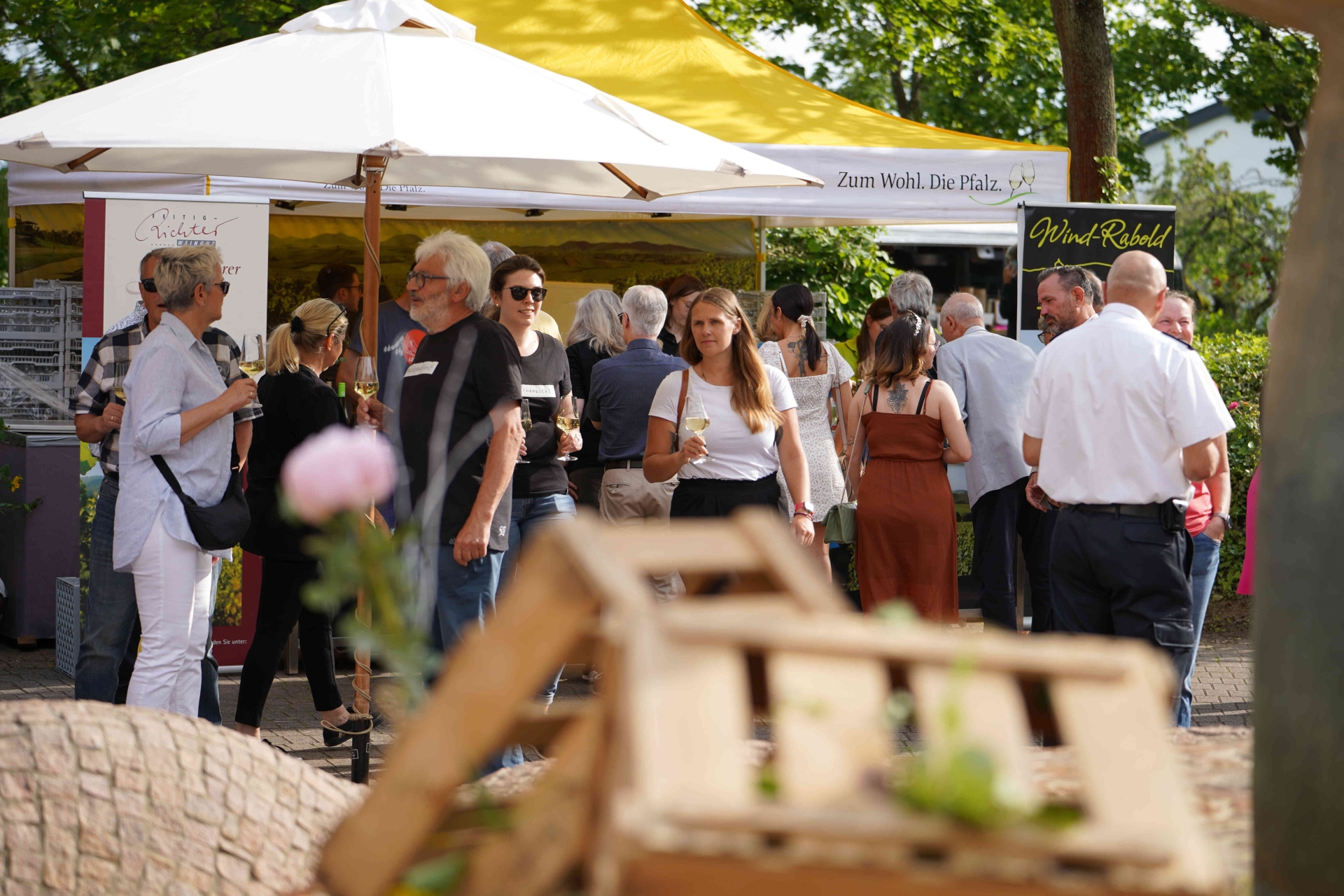 Menschen flanieren mit Stilgläsern in der Hand, im Hintergrund Pagodenzelte, im Vordergrund Weinkisten.