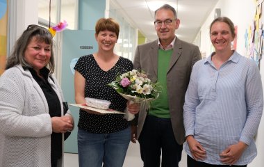 Gruppenbild: Von links nach rechts: Hannelore Schlageter (Leiterin Kreisjugendamt), Carmen Hüther (Kita-Leiterin), Georg Kern (Erster Kreisbeigeordneter) und Anna Groneß (Fachberaterin Kindertagesstätten beim Kreisjugendamt). Carmen Hüther hält einen Blumenstrauß sowie ein kleines Präsent in Händen. Alle lächeln in die Kamera.