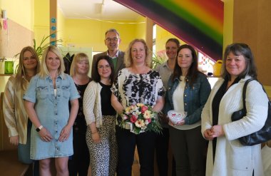 Gruppenbild mit mehreren Frauen und einem Mann in der Kita Böchingen. Eine Frau hält einen Blumenstrauß in der Hand, eine weitere ein Präsent mit der Aufschrift Herzlichen Dank. Das "Herz" ist dabei nicht ausgeschrieben, sondern mit einem roten Herz dargestellt.