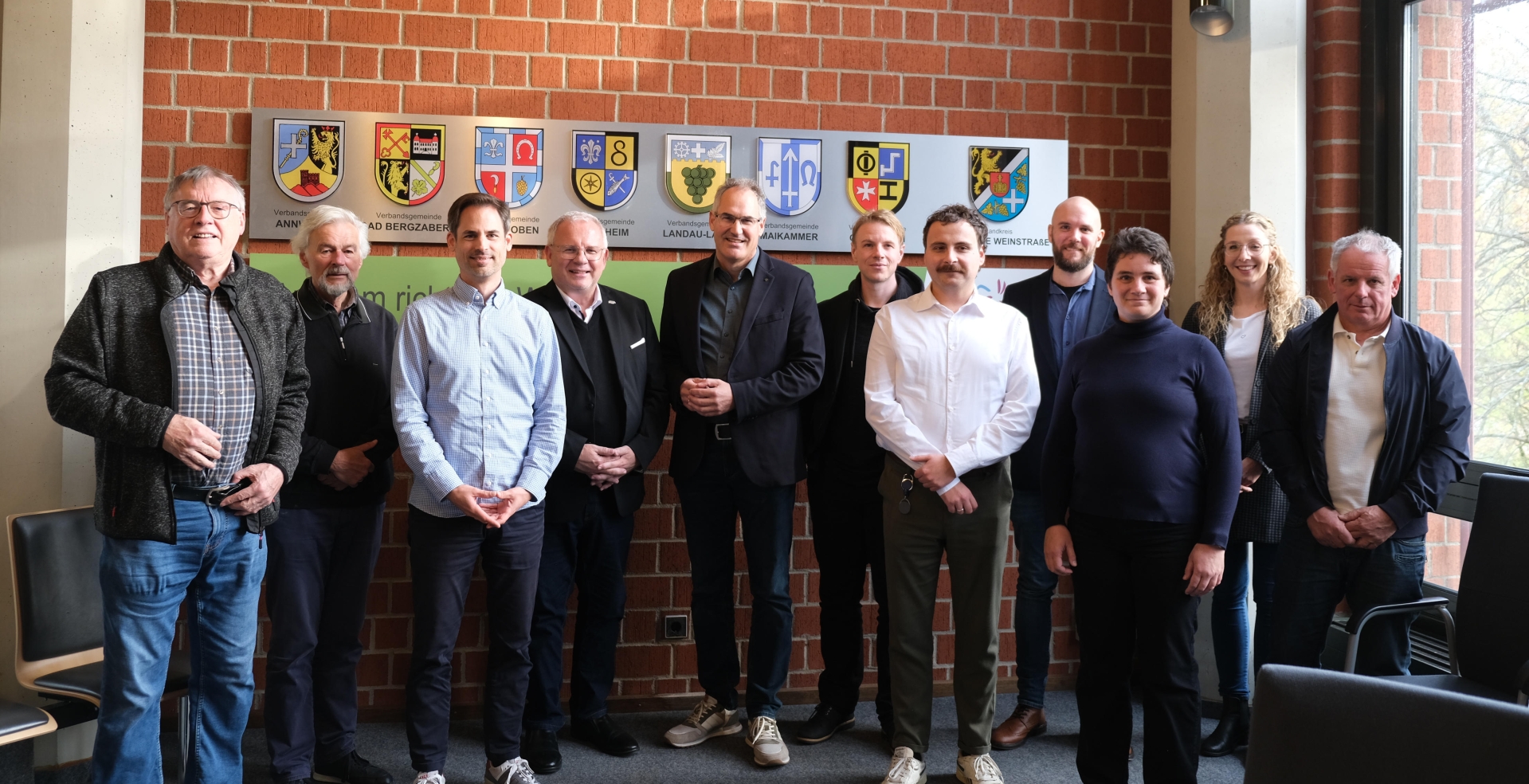 Gruppenfoto: Die Beteiligten der Beiratssitzung stehen vor einer Ziegelwand im Kreishaus Südliche Weinstraße.
