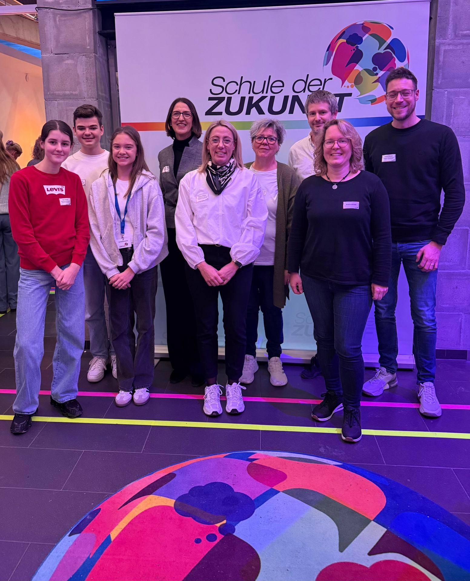 Gruppenbild: Schülerinnen, Schüler und Lehrkräfte der Realschule plus im PAMINA-Schulzentrum Herxheim mit Schulleiterin Magdalena Mayer. Im Hintergrund ist ein Rollup mit der Aufschrift "Schule der Zukunft" zu sehen.