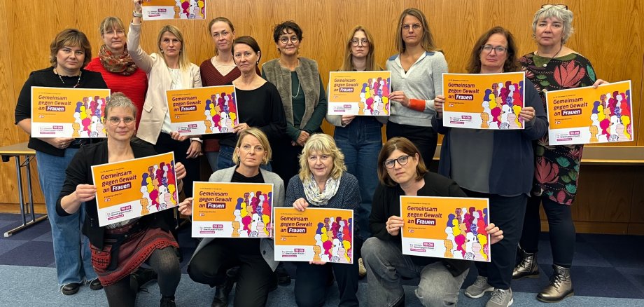 Gemeinsam für Geschlechtergerechtigkeit: Die Landesarbeitsgemeinschaft (LAG) der kommunalen Frauen- und Gleichstellungsbeauftragten hat sich Ende Oktober zu ihrer Herbstsitzung im Landkreis Südwestpfalz getroffen. Mit dabei war auch die SÜW-Gleichstellungsbeauftragte Isabelle Stähle (untere Reihe, Zweite von links). Foto: KV Südwestpfalz Eine Gruppe von Frauen hält Plakate mit der Aufschrift „Gemeinsam gegen Gewalt an Frauen“ in die Kamera. Die Gruppe steht in einem Raum mit Holzwand.