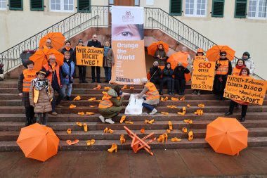 Der Zonta Club Bad Bergzabern mit seiner „Mensch-Kunstinstallation“ mit dem Titel „Zonta Says No – WIR schauen NICHT weg!“ vor der Verbandsgemeindeverwaltung Bad Bergzabern. Foto: Wolfgang Faber Mehrere Personen stehen und sitzen auf der Treppe vor dem Schloss Bad Bergzabern mit Bannern, Plakaten und zahlreichen orangefarbenen Schuhen. Auf den Plakaten steht „Wir schauen nicht weg“ und „Zonta sagt Nein zu Gewalt an Frauen“.