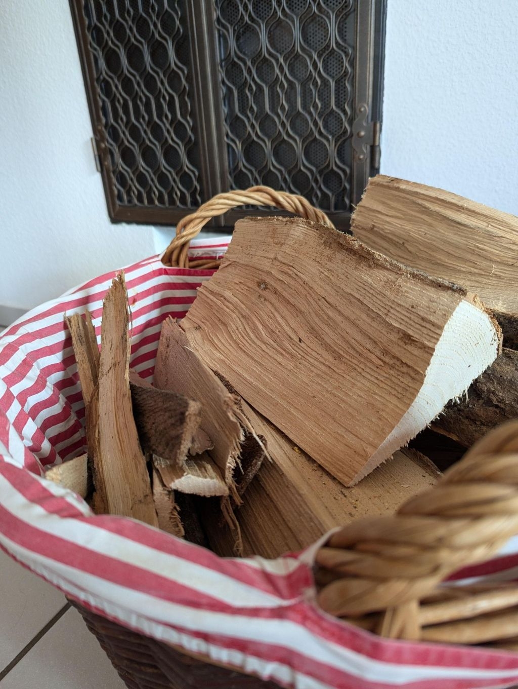 Holzscheite liegen in einem Weidenkorb, der mit einem rot-weiß gestreiften Stoff ausgekleidet ist. 