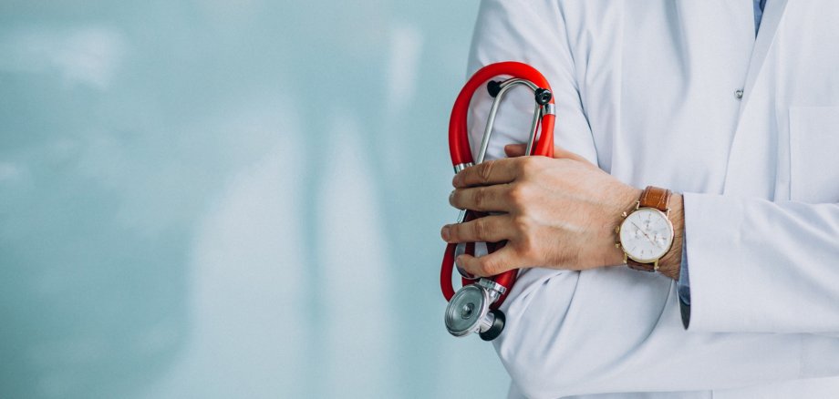 Nahaufnahme eines Arztes in typischem weißen Kittel, der ein Stethoskop hält. Es ist nur der Oberkörper, kein Gesicht, zu sehen.