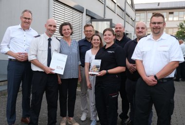 Mehrere Personen im Halbkreis, zwei Menschen halten je eine Urkunde und eine Stele, den Preis, in der Hand.