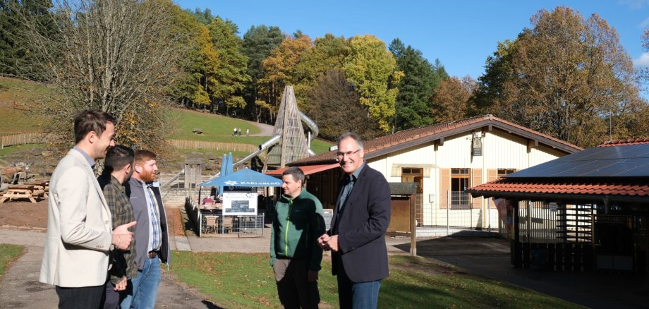 Fünf Männer stehen im Grünen, dahinter zwei Gebäude und eine Riesenrutsche.