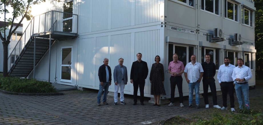 Mehrere Personen stehen vor einem zweigeschossigen weißen Containergebäude mit Außentreppe. Die Gruppe posiert für ein Foto im  Außenbereich des PAMINA-Schulzentrums in Herxheim.