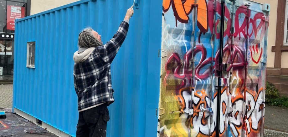 Frank Cmuchal gestaltet die Galerie mobil derzeit um, und zwar in Wissembourg. Foto: Karlheinz Zwick Ein Künstler sprayt einen Überseecontainer mit blauer Farbe an. Auf einer anderen Seite des Containers ist der Schriftzug "Europa" als Graffiti zu lesen.