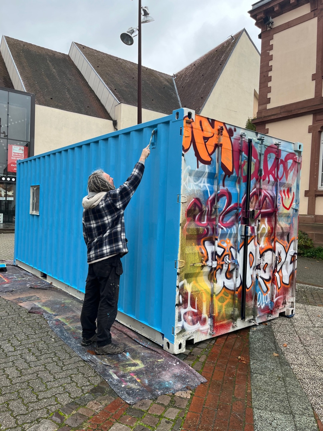 Frank Cmuchal gestaltet die Galerie mobil derzeit um, und zwar in Wissembourg. Foto: Karlheinz Zwick Ein Künstler sprayt einen Überseecontainer mit blauer Farbe an. Auf einer anderen Seite des Containers ist der Schriftzug "Europa" als Graffiti zu lesen.