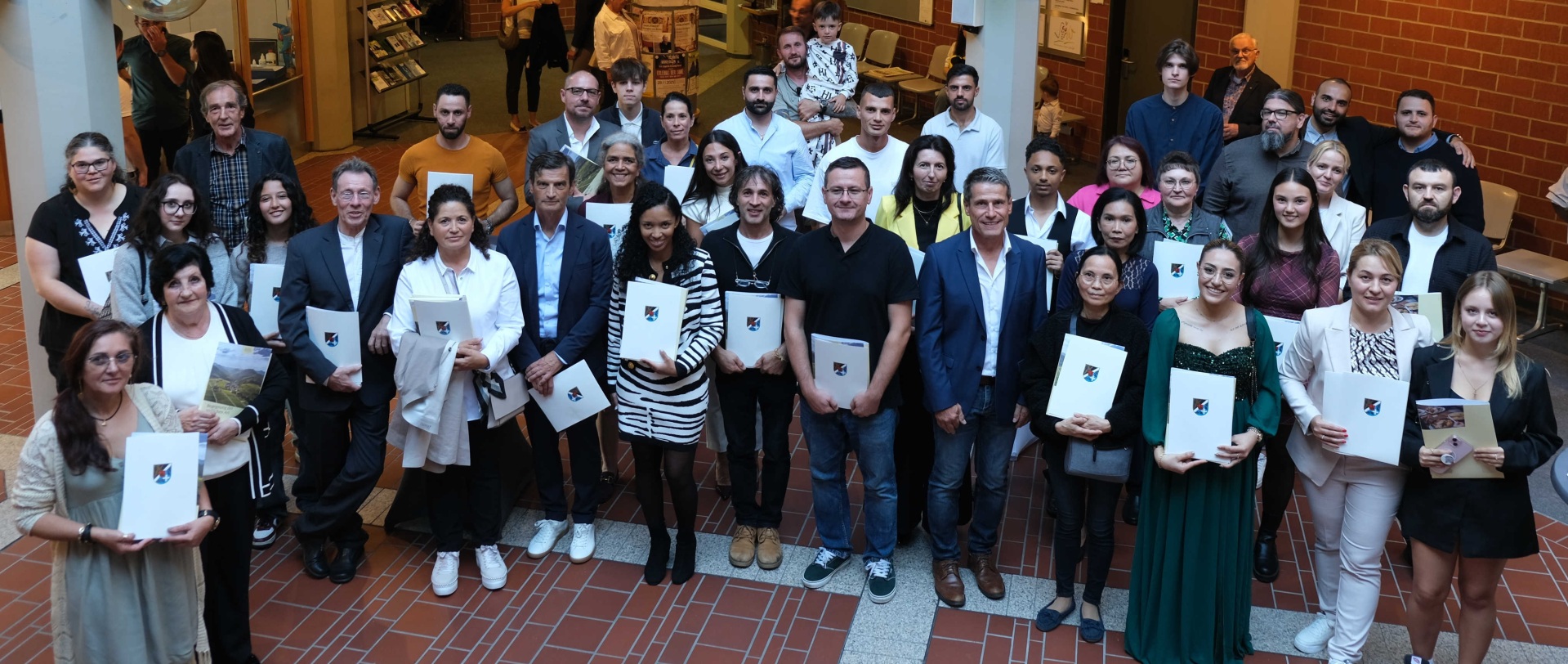 Gruppenbild: 39 neue deutsche Staatsbürgerinnen und Staatsbürger stehen im Foyer des Kreishauses SÜW, mit Kreisbeigeordnetem Uwe Huth, Mitarbeitenden der Verwaltung und Gästen.