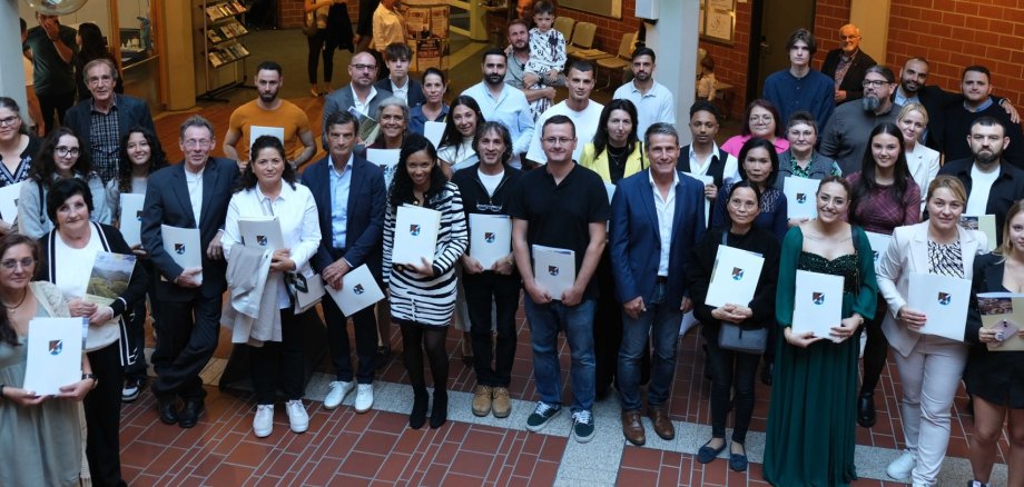 Gruppenbild: 39 neue deutsche Staatsbürgerinnen und Staatsbürger stehen im Foyer des Kreishauses SÜW, mit Kreisbeigeordnetem Uwe Huth, Mitarbeitenden der Verwaltung und Gästen.