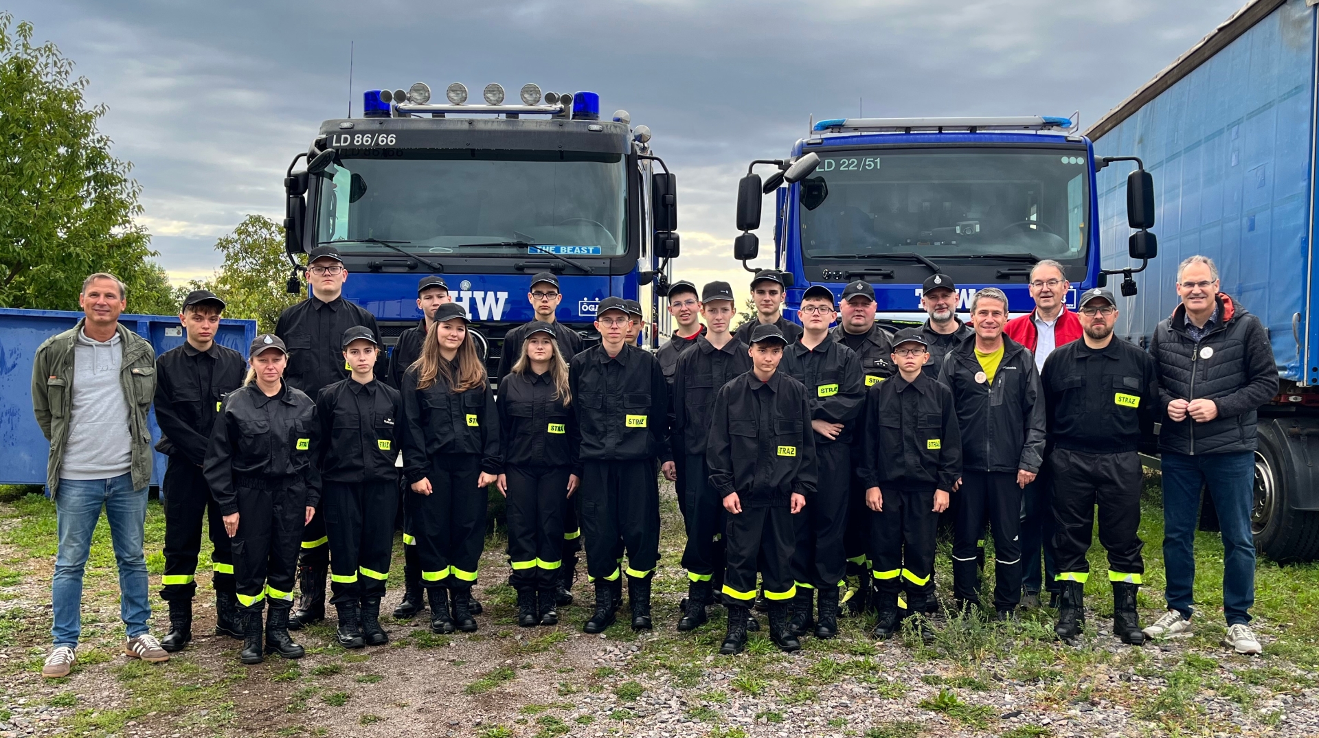 Gruppenbild: Mitglieder einer Jugendfeuerwehr aus dem polnischen Oświęcim stehen vor zwei Fahrzeugen des THW. Sie tragen schwarze Uniformen mit neongelben Leuchstreifen an den Hosenbeinen. Mit in der Gruppe stehen Landrat Dietmar Seefeldt , der Erste Kreisbeigeordnete Georg Kern, Kreisbeigeordneter Uwe Huth und Organisator Heiko Pabst.
