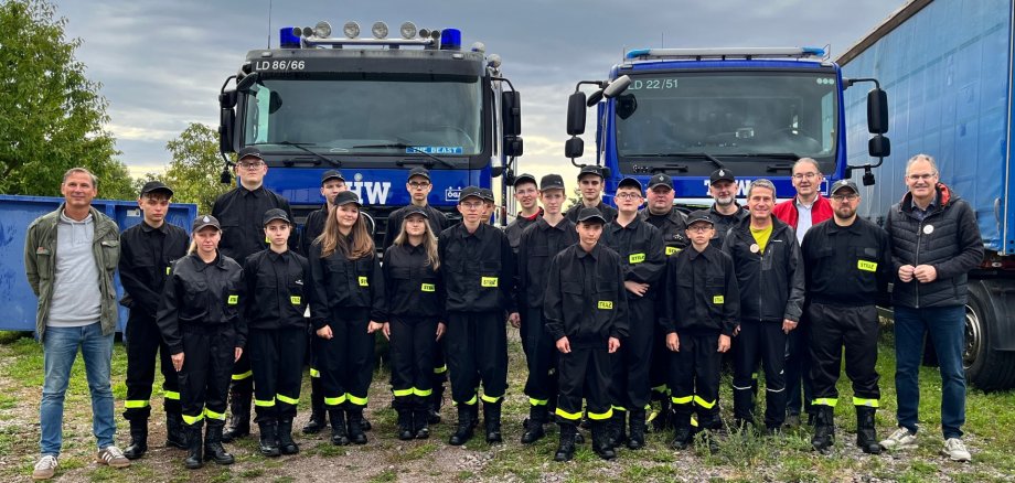 Gruppenbild: Mitglieder einer Jugendfeuerwehr aus dem polnischen Oświęcim stehen vor zwei Fahrzeugen des THW. Sie tragen schwarze Uniformen mit neongelben Leuchstreifen an den Hosenbeinen. Mit in der Gruppe stehen Landrat Dietmar Seefeldt , der Erste Kreisbeigeordnete Georg Kern, Kreisbeigeordneter Uwe Huth und Organisator Heiko Pabst.