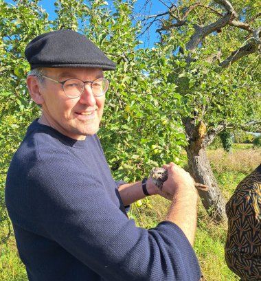 Erster Kreisbeigeordneter Georg Kern steht auf einer Streuobstwiese neben niedrigen Bäumen und hält einen jungen Steinkauz in der Hand.
