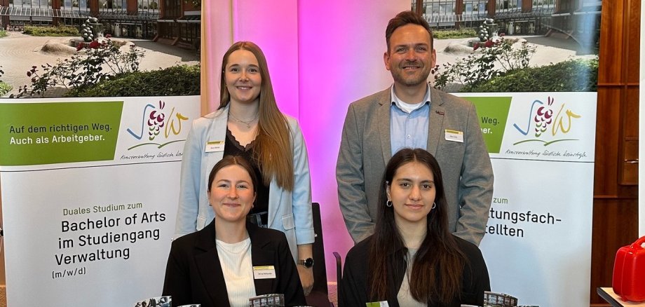 Vier Personen aus dem Team der Kreisverwaltung SÜW an einem Messestand. Auf einem Tisch liegen Info-Flyer. Im Hintergrund sind zwei Rollups zu sehen, die das duale Studium und die Ausbildung bei der Kreisverwaltung bewerben.
