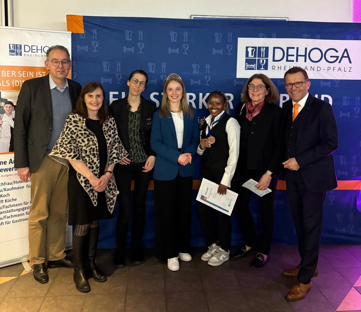 Sieben Personen stehen vor einer DEHOGA-Rheinland-Pfalz-Fotowand und lächeln in die Kamera.