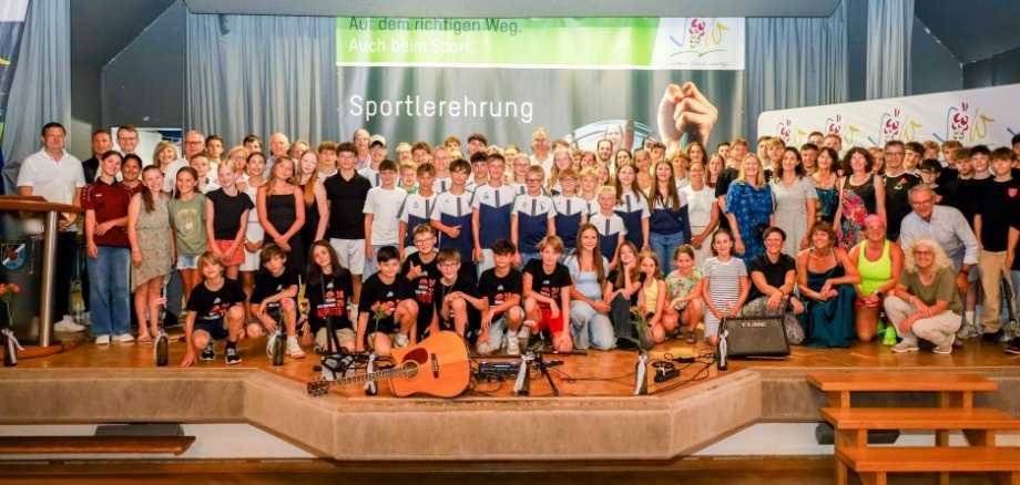 Auf einer Bühne stehen zahlreiche Sportlerinnen und Sportler in schicker Kleidung, die in die Kamera lächeln.