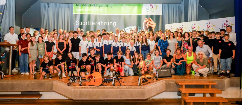 Auf einer Bühne stehen zahlreiche Sportlerinnen und Sportler in schicker Kleidung, die in die Kamera lächeln.