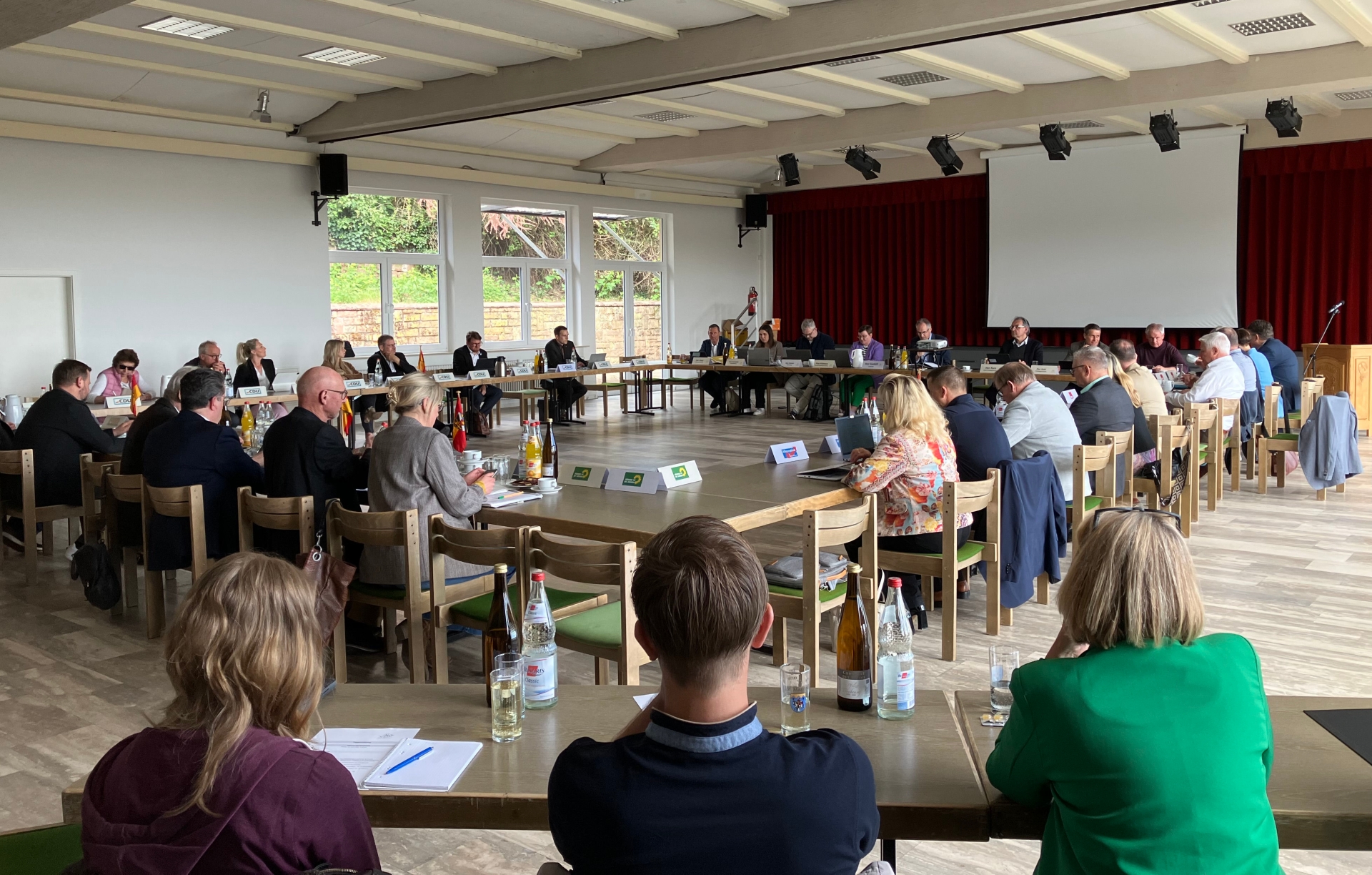 Blick in den Kreistag. Die versammelten Mitglieder sitzen in einem hellen Saal an im Quadrat angeordneten Tischen.