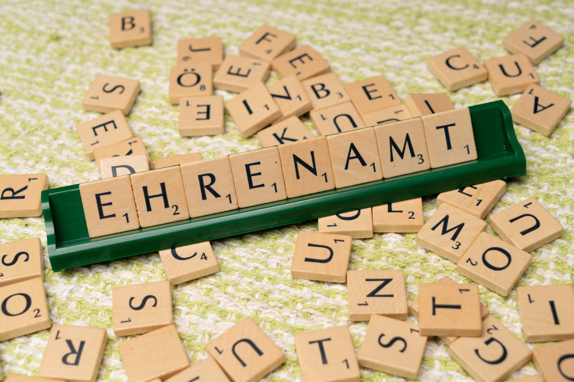 Auf einem Scrabble Board ist mit Buchstaben-Spielsteinen das Wort "Ehrenamt" zusammengesetzt.