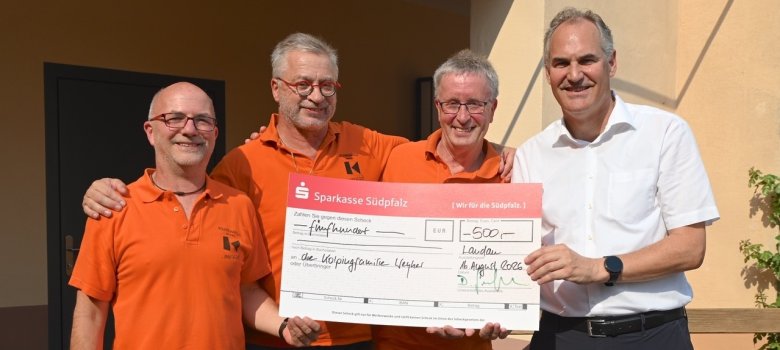 Spendenübergabe an die Kolping-Kapelle Weyher. Foto: Richard Zinken/frei Vier Männer stehen nebeneinander und lächeln in die Kamera. Drei von ihnen tragen orangefarbene Poloshirts. gemeinsam präsentieren sie einen Spendenscheck der Sparkasse Südpfalz über 500 Euro für die Kolpingfamilie Weyher.