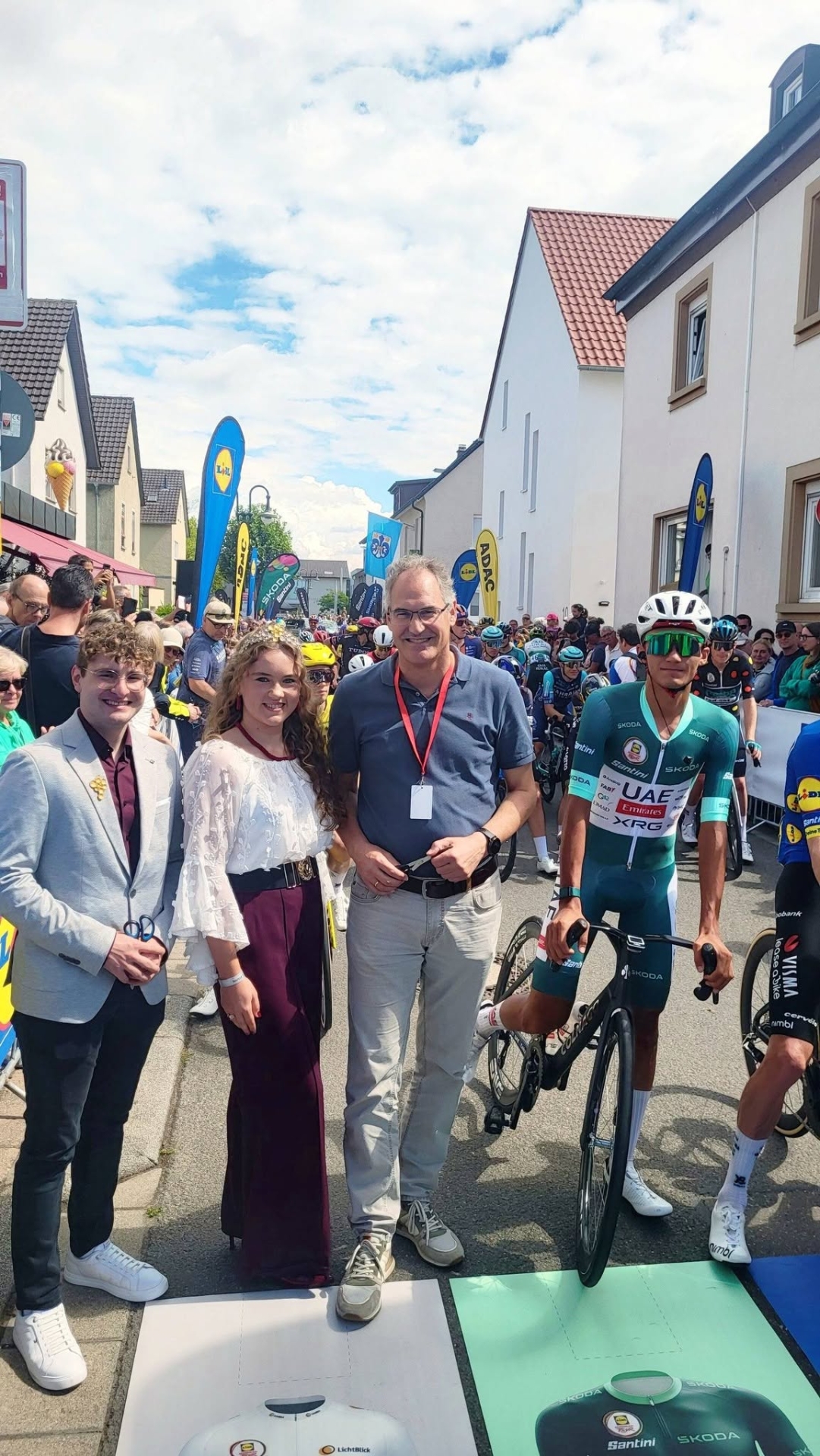 Vier Personen, einer davon auf einem Rennrad in Sportkleidung, eine mit Krone.
