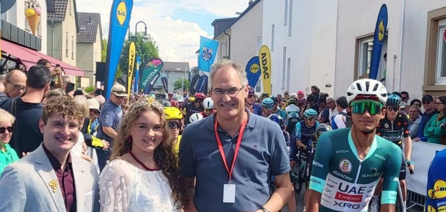 In Herxheim am Samstag, kurz vor Start der dritten Etappe der Deutschland-Tour: SÜW-Weinhoheiten Johannes Keller (links) und Klaudia Göpel mit Landrat Dietmar Seefeldt und dem späteren Tour-Gewinner Isaac Del Toro aus Mexiko. Foto: Seefeldt Vier Personen, einer davon auf einem Rennrad in Sportkleidung, eine mit Krone.