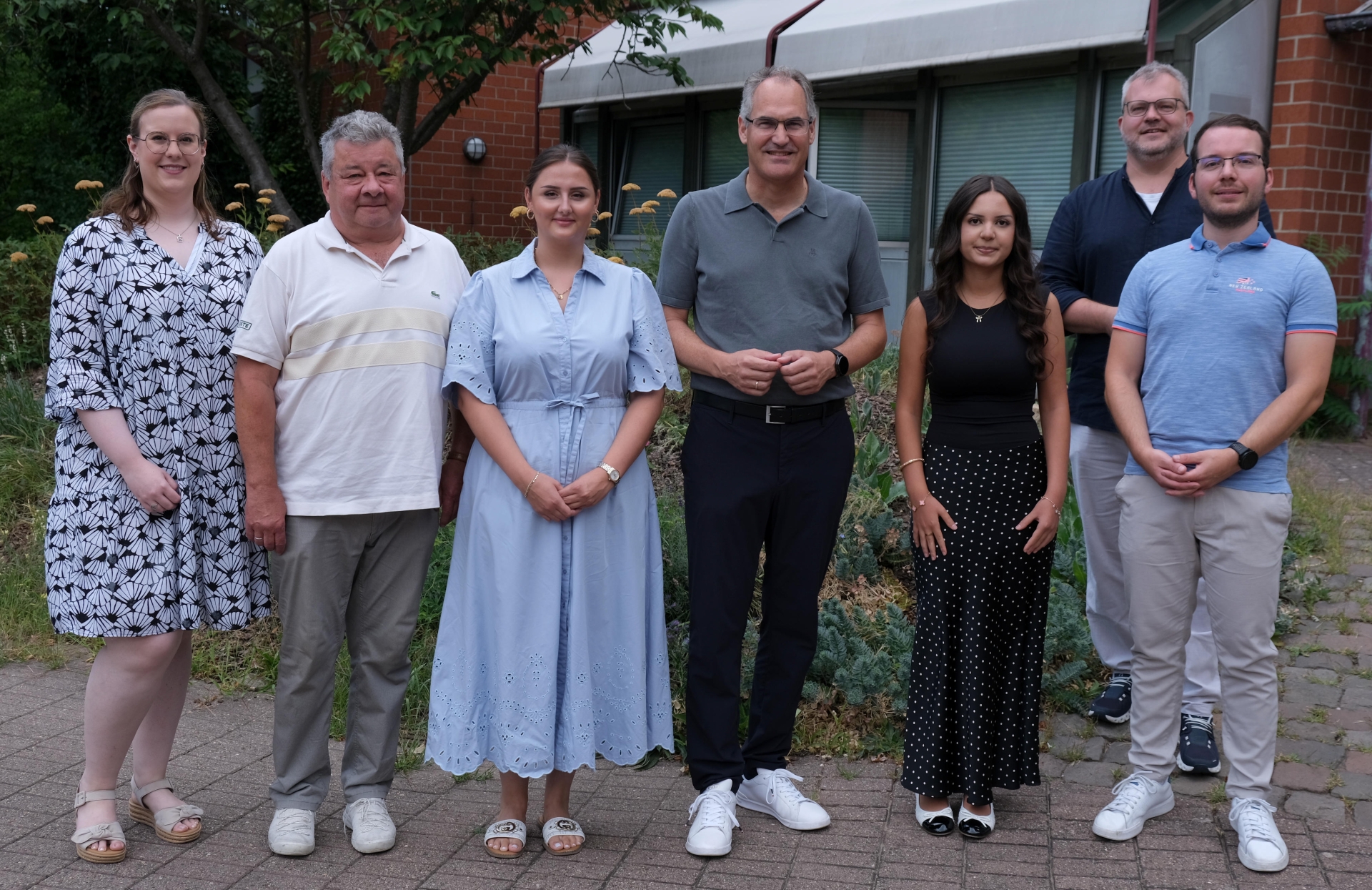 Sieben Personen stehen für ein Gruppenfoto vor einem Gebäude.