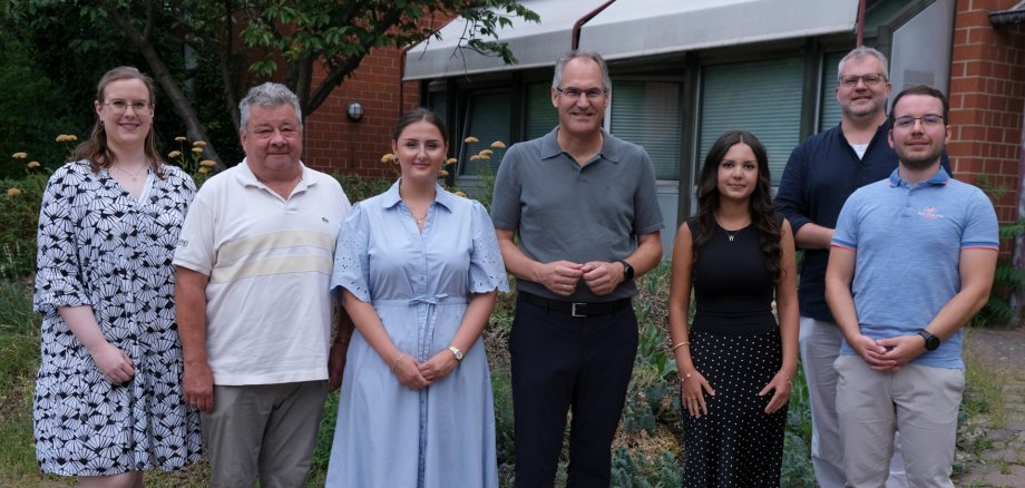Sieben Personen stehen für ein Gruppenfoto vor einem Gebäude.