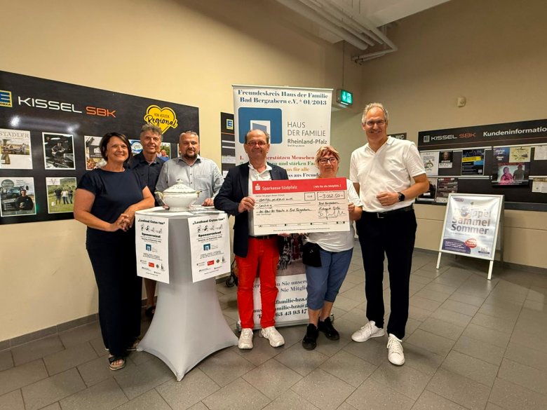 Sechs Personen stehen in einem Supermarkt für ein Gruppenfoto zusammen. Zwei von ihnen halten einen großen Spendenscheck.