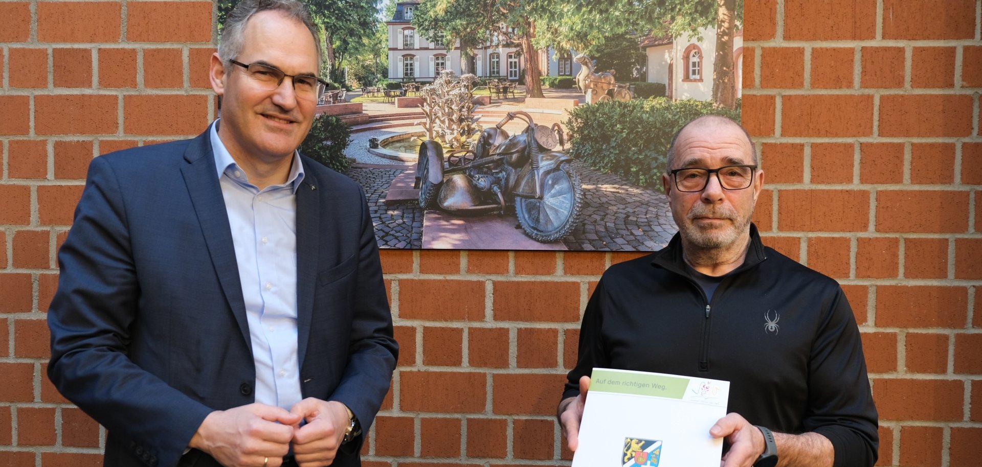 Landrat Dietmar Seefeld und Amtstierarzt Burkhard Prill vor einer Ziegelwand im Kreishaus der Südlichen Weinstraße.