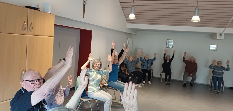Menschen sitzen im Kreis und strecken die Arme hoch.
