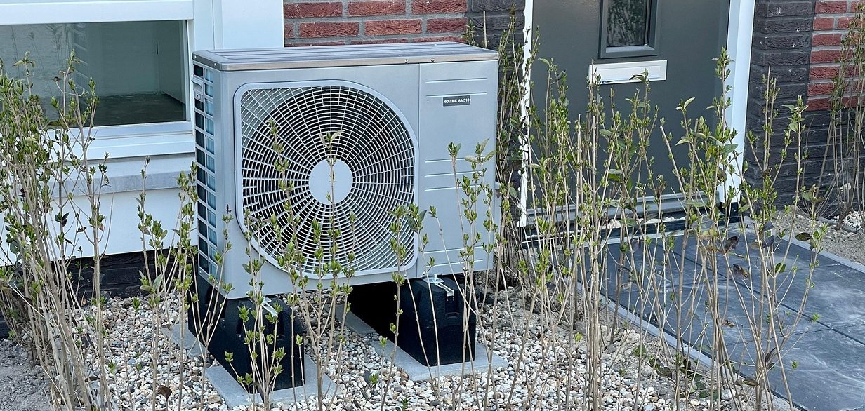 Eine Wärmepumpe vor einem Hauseingang.