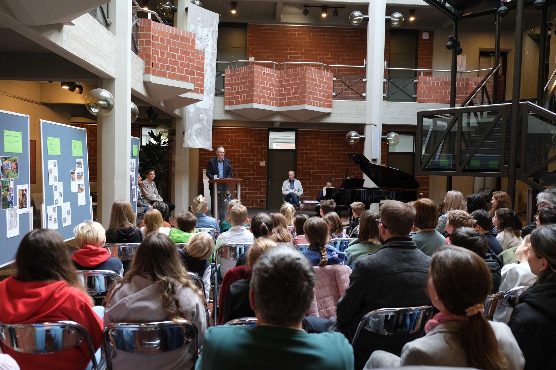 Eine Gruppe von Kindern und Erwachsenen sitzt auf Stühlen vor einem Rednerpult und Stellwänden.