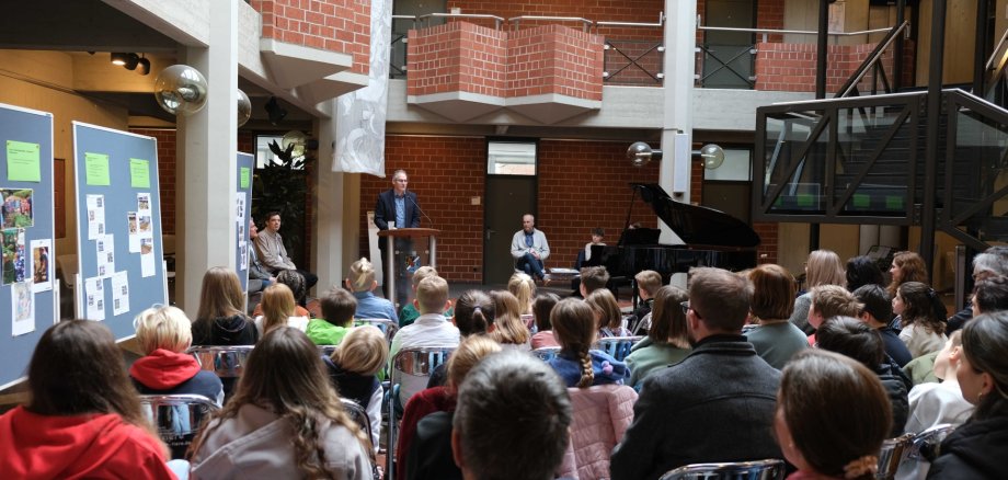 Eine Gruppe von Kindern und Erwachsenen sitzt auf Stühlen vor einem Rednerpult und Stellwänden.