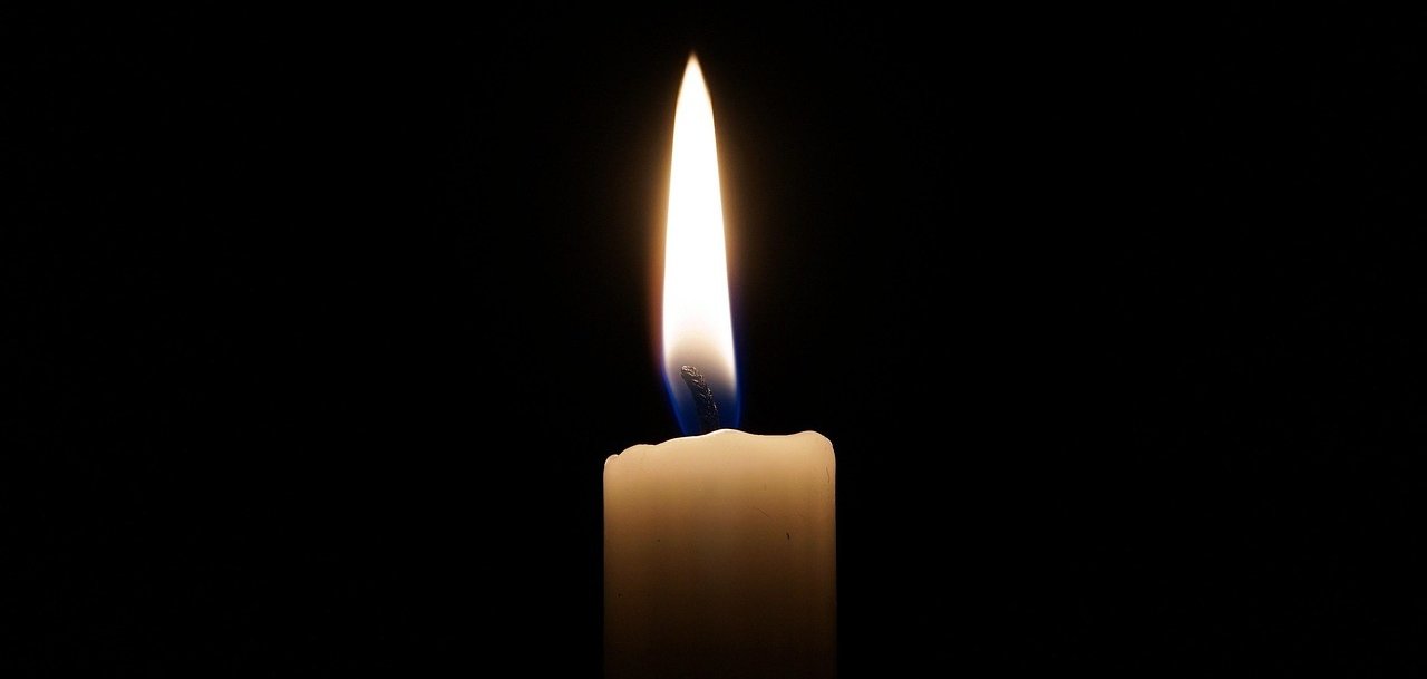 Eine einzelne brennende Kerze vor schwarzem Hintergrund.