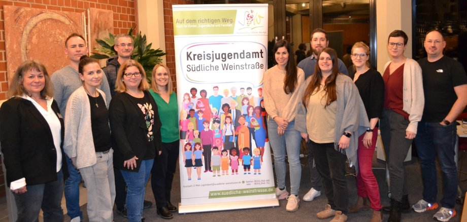 Gruppenbild: 12 Personen stehen links und rechts von einem Rollup des Kreisjugendamts Südliche Weinstraße.
