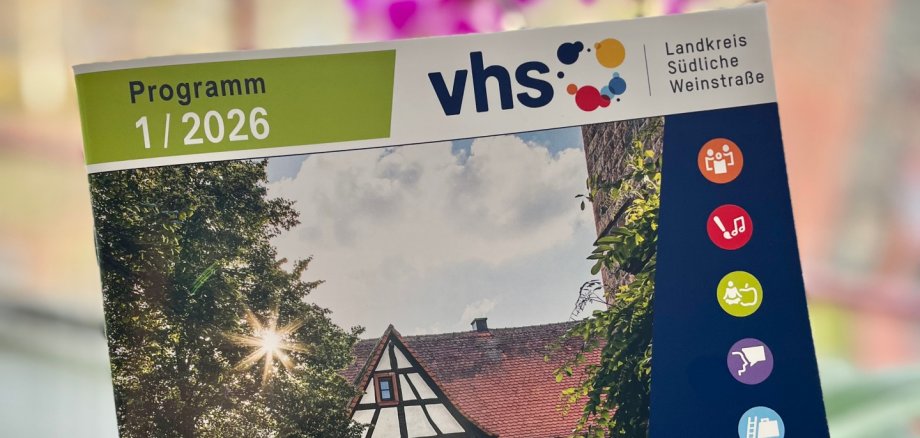 Das Titelfoto zum neuen Programmheft der Kreisvolkshochschule hat Klaus Forstner aus Klingenmünster aufgenommen. Foto: KV SÜW Eine Hand hält das neue Programmheft der kvhs SÜW, im Hintergrund unscharf eine Orchidee.