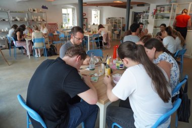Beim Azubi-Tag im Keramik-Malstudio TonArt in Landau war die Kreativität der angehenden Verwaltungsfachangestellten, Verwaltungsbeamtinnen und -beamten sowie Sozialarbeiterinnen gefragt. Foto: KV SÜW Mehrere Menschen sitzen in Gruppen in einem Atelier an mehreren Tischen und bemalen Keramik.
