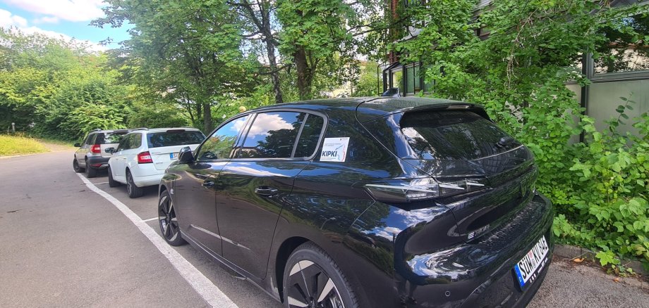 Ein schwarzes Auto steht auf einem Parkplatz, im Hintergrund das Kreishaus SÜW in Landau.