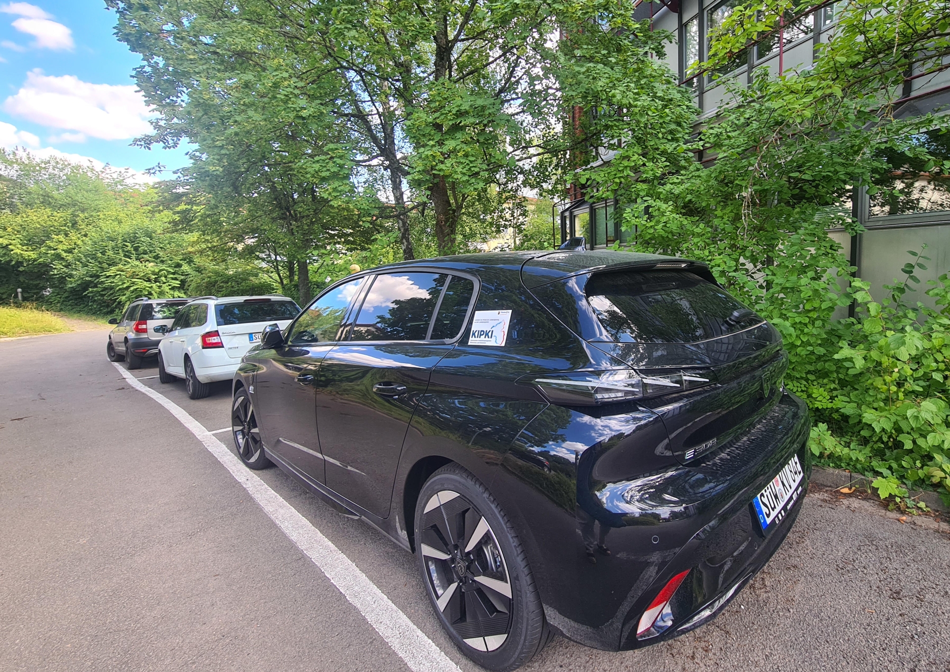 Ein schwarzes Auto steht auf einem Parkplatz, im Hintergrund das Kreishaus SÜW in Landau.
