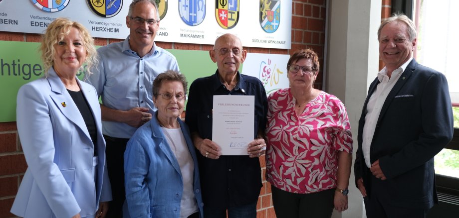 Bei der Feierstunde im Kreishaus von links nach rechts: Annweilers Stadtbürgermeisterin Carmen Winter, Landrat Dietmar Seefeldt, Hannelore Bastian, Horst Bastian, Petra Herbert (Gast) und Werner Kempf, Erster Beigeordneter der Verbandsgemeinde Annweiler am Trifels. Foto: KV SÜW Sechs Personen stehen vor einer Wappenwand.