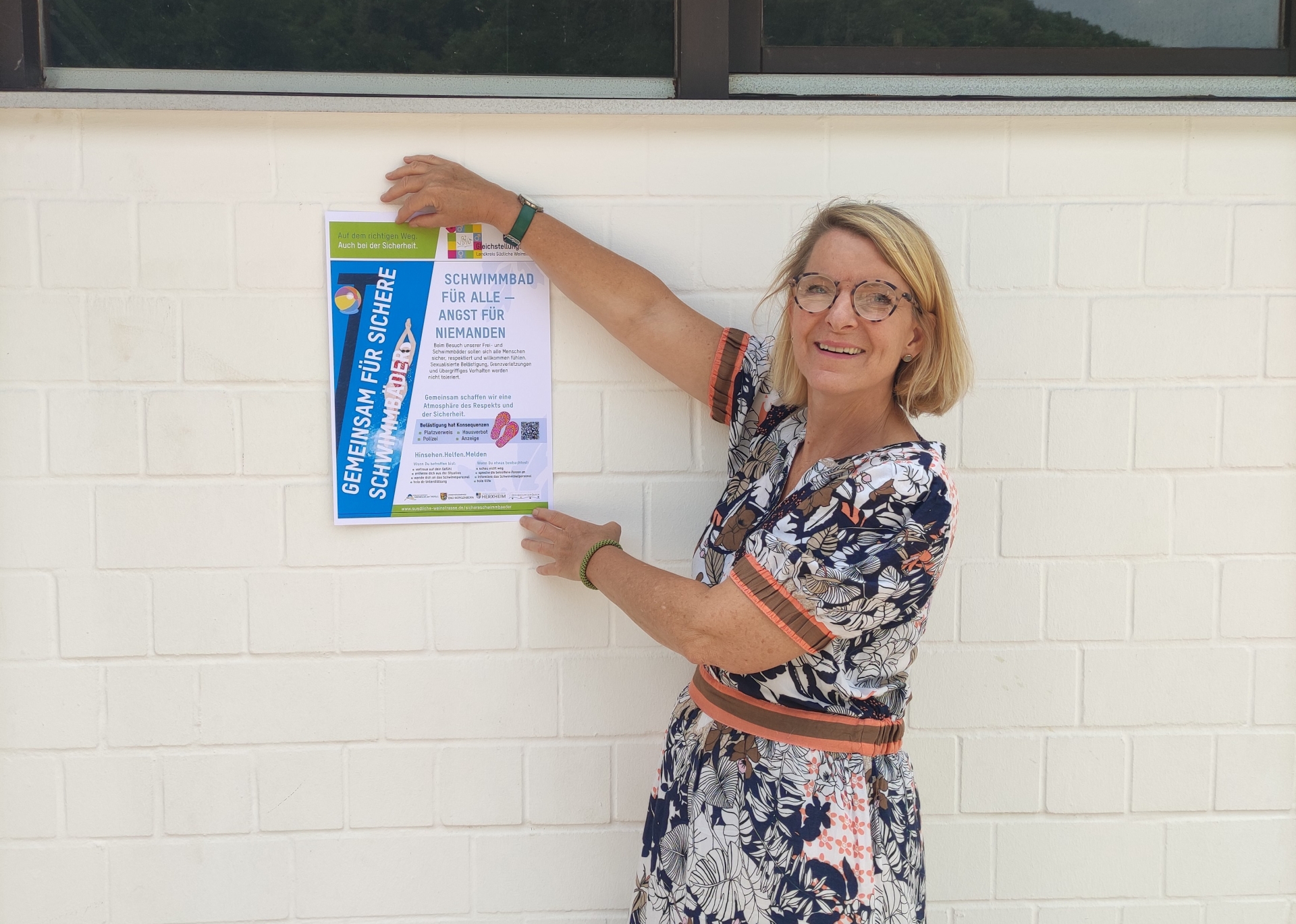 Die SÜW-Gleichstellungsbeauftragte Isabelle Stähle hat an einer weißen Wand im Trifelsbad in Annweiler ein Plakat zum Thema Sicherheit in Schwimmbädern angebracht.